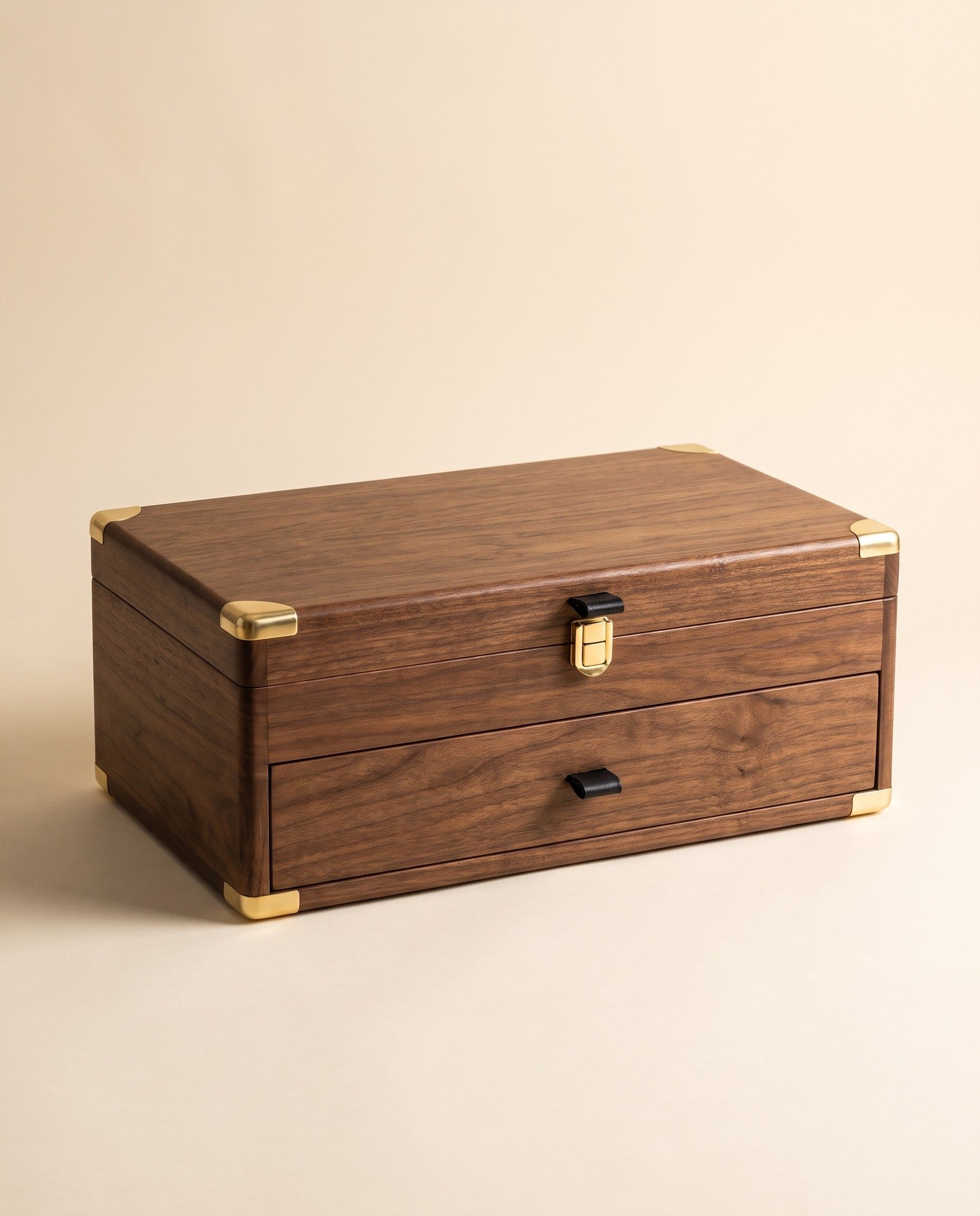 The closed walnut chest that holds an ĀBHĀ set, on a warm studio ground: a lidded upper tier with a gold-toned catch, a drawer below with a black pull, and gold-toned corner guards
