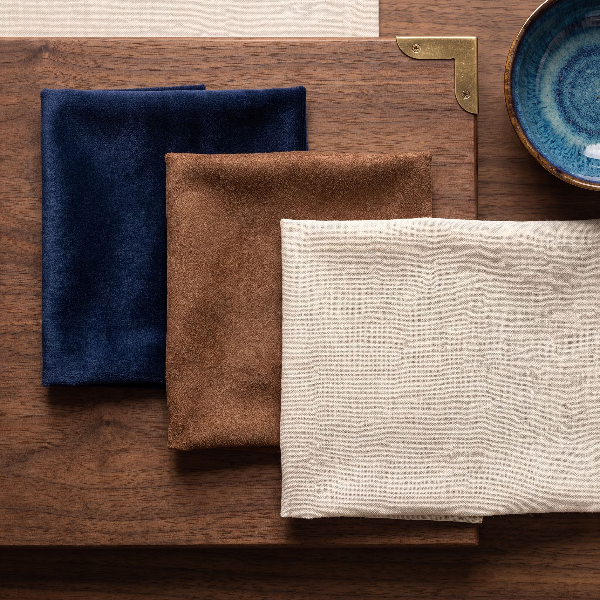 Three lining samples laid on walnut: indigo velvet, walnut-brown suede and ivory linen